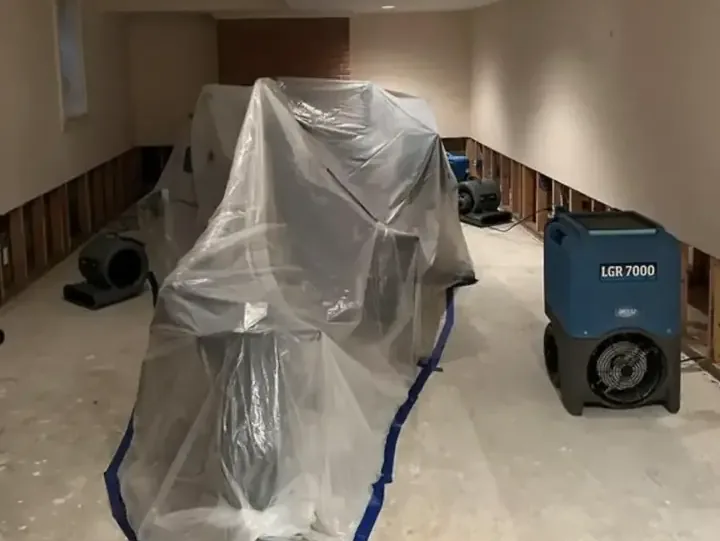 Plastic covers furnishings beside drying equipment and exposed lower wall framing