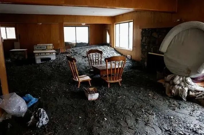 Mud and debris cover a furnished room after floodwater has receded