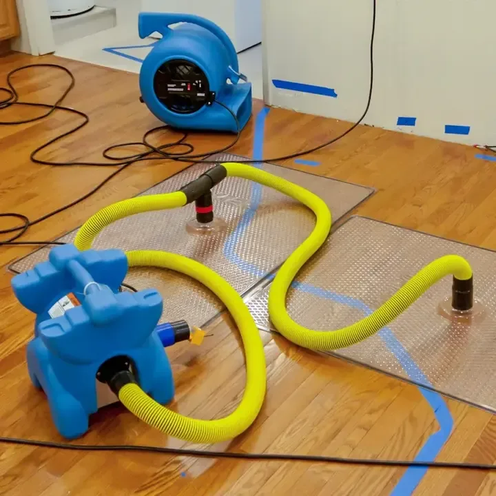 Yellow hoses connect floor drying mats to blue equipment on hardwood flooring