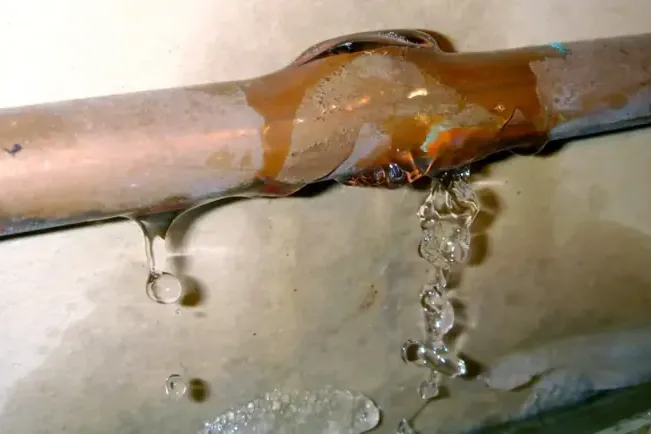 Water streams from a damaged copper pipe with corrosion around the opening