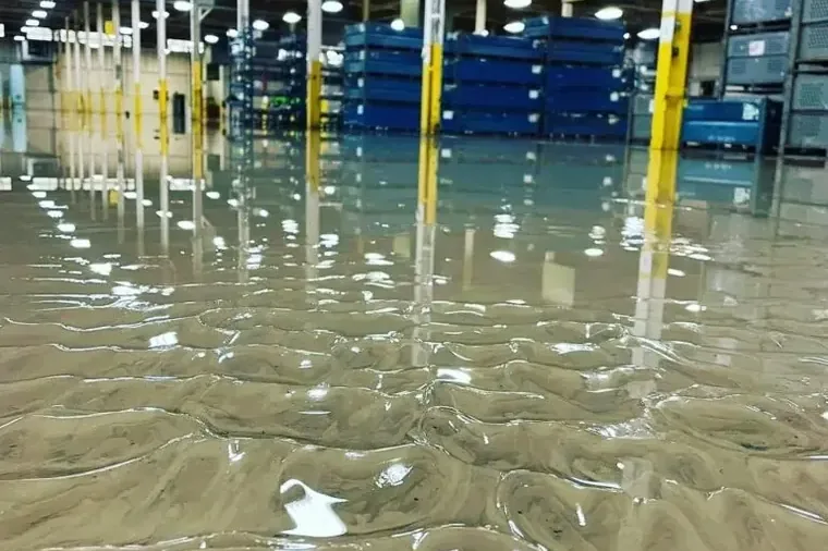 Standing water covers a warehouse floor beneath storage racks and yellow columns