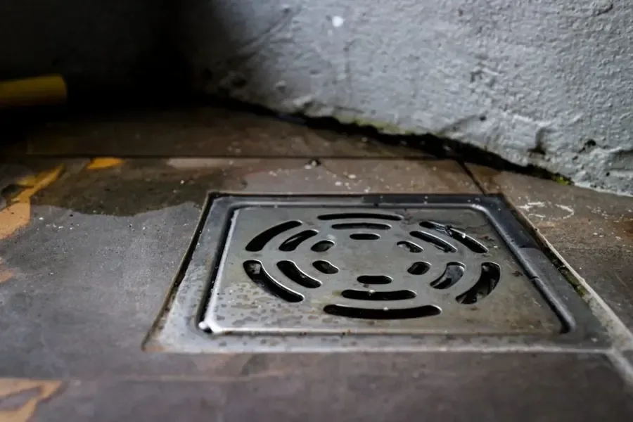 A metal floor drain sits in wet concrete beside a wall
