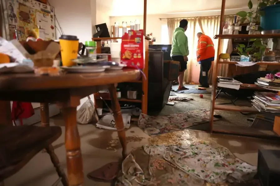 Workers stand in a living room with debris scattered across the floor